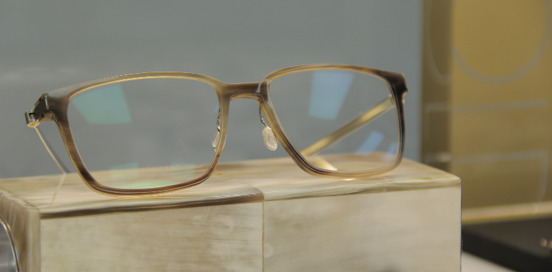 A pair of acetate LINDBERG glasses on display on top of a wooden block.]