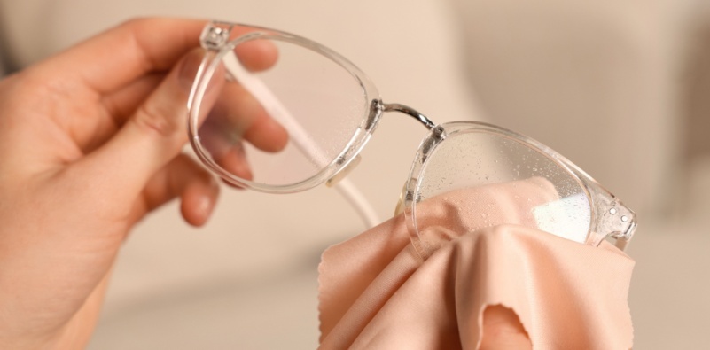 A woman cleaning her glasses with a microfibre cloth at home