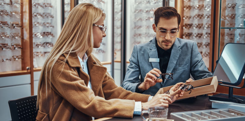 A woman choosing new glasses at the opticians, assisted by a male dispensing optician.