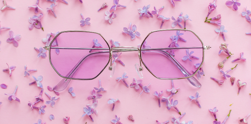 Silver sunglasses with lilac lenses on a floral pink background.