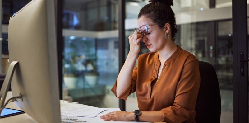 A woman wearing glasses rubbing the bridge of her nose at her desk