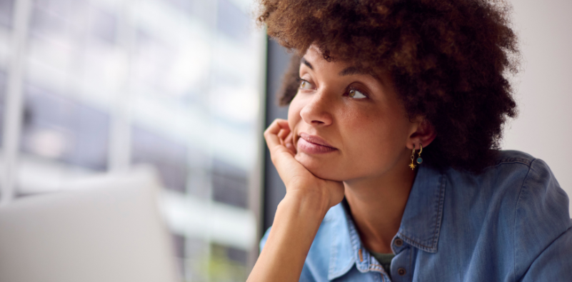 A woman resting her chin on her hand while looking away from a laptop