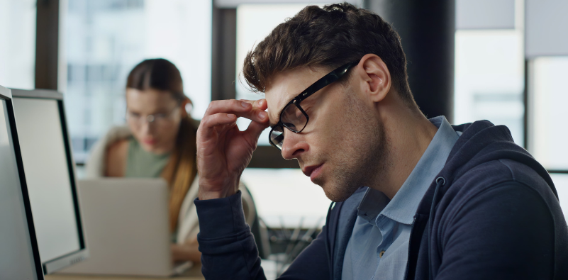 Man wearing glasses rubbing his forehead while working at a computer