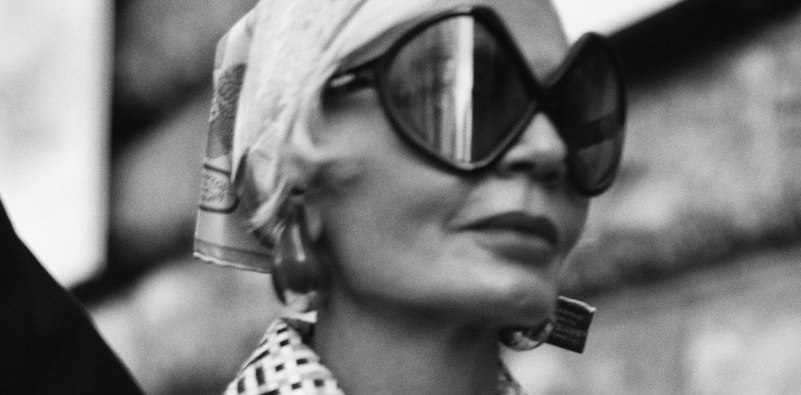 Black-and-white portrait of a woman in oversized sunglasses and a headscarf.